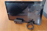 Front view of Samsung tablet with power adapter and cable placed in front of it on wood floor.