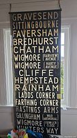 Full view of antique fabric wall hanging with train station names including Gravesend, Sittingbourne, Faversham, and others in white and gold lettering on black fabric.