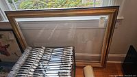 Full view of the large wooden picture frame leaning against a window with the silverware set in front of it.