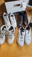 Four pairs of men's size 6 shoes: two white Nike sneakers including a high-top and Vapormax, brown leather dress shoes, and white mesh athletic sneakers arranged on wooden floor.