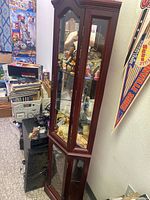 Full view of tall dark wood curio cabinet with glass front and side panels, showing the interior filled with clown figurines, no visible damage to glass or wood