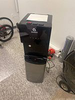 Front view of the Avalon water filtration dispenser showing black and silver finish with the Avalon logo on the front panel, standing upright.