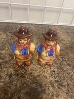 Full view of both cowboy salt and pepper shakers standing side by side on a countertop, showing overall shape and color.