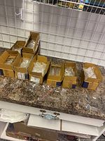 Several cardboard boxes filled with individually wrapped clear glass Christmas ornaments on a countertop.