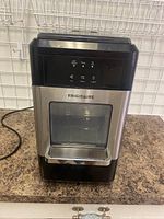 Front view of the Frigidaire portable ice maker showing stainless steel front, touch controls, and ice dispensing window.