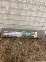 Roll of galvanized hardware cloth on a countertop against a wire grid wall, showing complete roll and packaging.