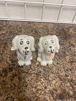 Front view of the pair of ceramic dog salt and pepper shakers placed on a brown countertop, showing the facial and bow tie details.