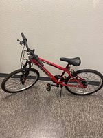 Side view of the red Huffy Highland mountain bike with visible 21-speed gear system and black pedals.