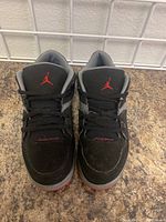 Front angle of both kids' Nike Air Jordan shoes showing black suede upper, red Jumpman logo on tongue and 'Jordan' text in red on toe area.