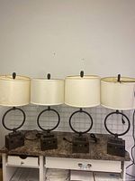 Photo of all four identical lamps showing circular metal frames with white fabric shades and dark square bases with outlets and switches.