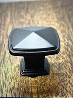 Close-up image of a single black oil rubbed metal square knob featuring a raised pyramid design on top with a beveled base.