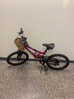 Full side view of the pink and black Magenta Hyper girls bike with front wicker basket, knobby tires, and kickstand down, showing overall condition.