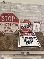 Full lot of four signs displayed on a counter against wire rack, showing different warning and notice signs.