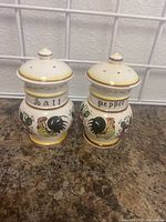 Pair of Royal Sealy ceramic salt and pepper shakers with rooster and floral decoration, cream color with yellow trim, labeled "Salt" and "Pepper".