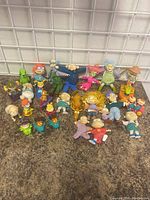 Full group of 28 Rugrats figurines and toys displayed on a countertop against a wire grid background.