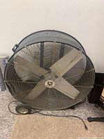 Front view of Strongway industrial floor fan showing four metal blades and protective wire guard, with visible dust and dirt on blades and grill.