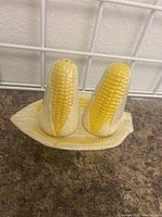 Salt and pepper shakers designed as corn on the cob, placed on matching corn-shaped base on a counter, shown from side angle