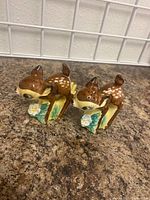 Front and side view of the two ceramic deer salt and pepper shakers with floral bases on a countertop.