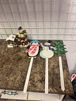 Photo of five Christmas decorations including a ceramic train station/snowman and four wooden garden stakes with winter holiday characters and tree