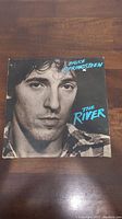 Front cover of Bruce Springsteen The River vinyl album, black and white photo of Bruce Springsteen with turquoise text.