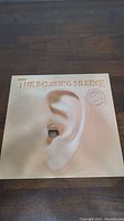 Front cover of The Roaring Silence vinyl album showing large ear artwork with a mouth inside, and album title embossed