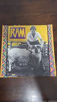 Front cover of the Ram album showing Paul McCartney with a ram and colorful border artwork.