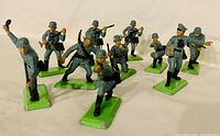 Photo of 10 vintage British WWII Britains LTD Deetail toy soldier figures standing on green bases, various poses including rifle firing, saluting, grenade throwing. All figures made of metal with detailed paint.