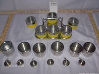 Set arrangement showing 6 yellow slip-proof tins in pyramid shape on triangular stainless steel tray, 6 stainless steel magnetic spice containers in front, 6 small magnetic hooks laid out in front.