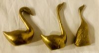 Three solid brass swan figurines displayed on white background showing varying neck postures and sizes