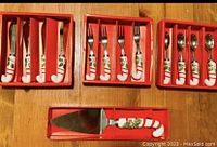 Top view of four boxes of Christmas-themed flatware sets arranged showing knives, forks, spoons, and cake server with handles decorated in red and white stripes with holly.