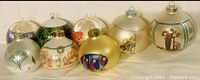 Photo showing 8 vintage large glass Christmas ornaments, various colors and holiday themed illustrations.