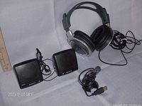 Stereo headphones, two small Sony speakers, and a small USB computer microphone, displayed together on light-colored fabric background with ruler for scale
