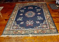 Full view of the rug from a distance showing blue central area, floral medallion, and intricate borders with fringe ends.
