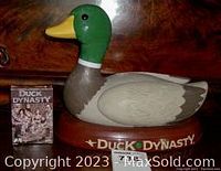 Front view of the Duck Dynasty talking mallard duck with DVD tape placed beside it on a wooden surface.