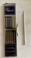 Front view of vintage metal Valiant personal calculator showing blue and silver slider controls for addition and subtraction alongside metal stylus.
