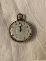 Front view of gold tone Cardinal pocket watch showing white dial with black numerals and hands