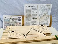 Photo of the Woodscape art kit showing basswood pieces with etched outlines, instruction sheets, and the box in the background