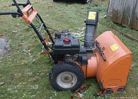 Side view of the orange Yard Machine snowblower showing front intake and chute, tires, handle with control panel.