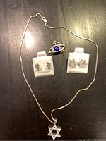 Photo showing the 16 inch sterling silver necklace with Star of David pendant, two pairs of sterling silver earrings on display holders, and a sterling silver bracelet with a blue eye design.