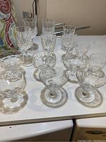 Top view showing variety of crystal glasses including tall wine glasses, flute glass, small stemmed glasses and stemless bowl glasses on white surface