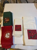 Photo of white bath towel with poinsettia applique alongside red towel with Santa Claus embroidery and green towels with Christmas scene embroidery.