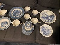 Overview of the blue and white china set showing cups, plates, a creamer, and a covered sugar bowl on a dark surface.