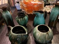 Photo showing Blue Mountain Pottery items including pitchers, vases, and bowls with green-blue dripped glaze on a table.