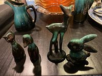 Five Blue Mountain pottery figurines (kitty, puppy, fawn, bunny) and a ceramic pitcher with blue and brown glaze on dark wood table.