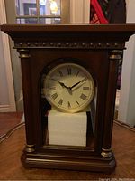 Wooden mantel clock with dark wood finish, gold-tone column accents and base, showing front view with clock face visible