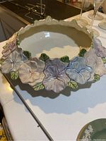 Top view of ceramic pansy bowl showing pink, blue, purple pansy flowers and green leaves around the rim, white interior.
