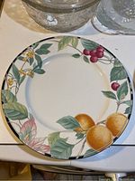 Full view of ceramic serving plate with fruit pattern including oranges, cherries, and leaves on white ceramic with dark rim.
