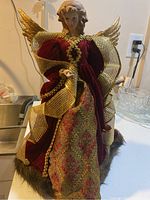 Front view of the Christmas angel figurine showing the detailed sculpted face, gold ribbon wings, and burgundy velvet dress with gold trim.