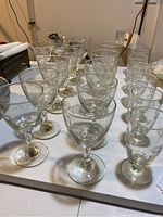 Wide view showing all 21 glasses arranged on a white surface, including wine, juice, and liquor glasses.