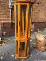 Full front side view of the tall oak-colored corner curio cabinet outdoors showing height and shape.